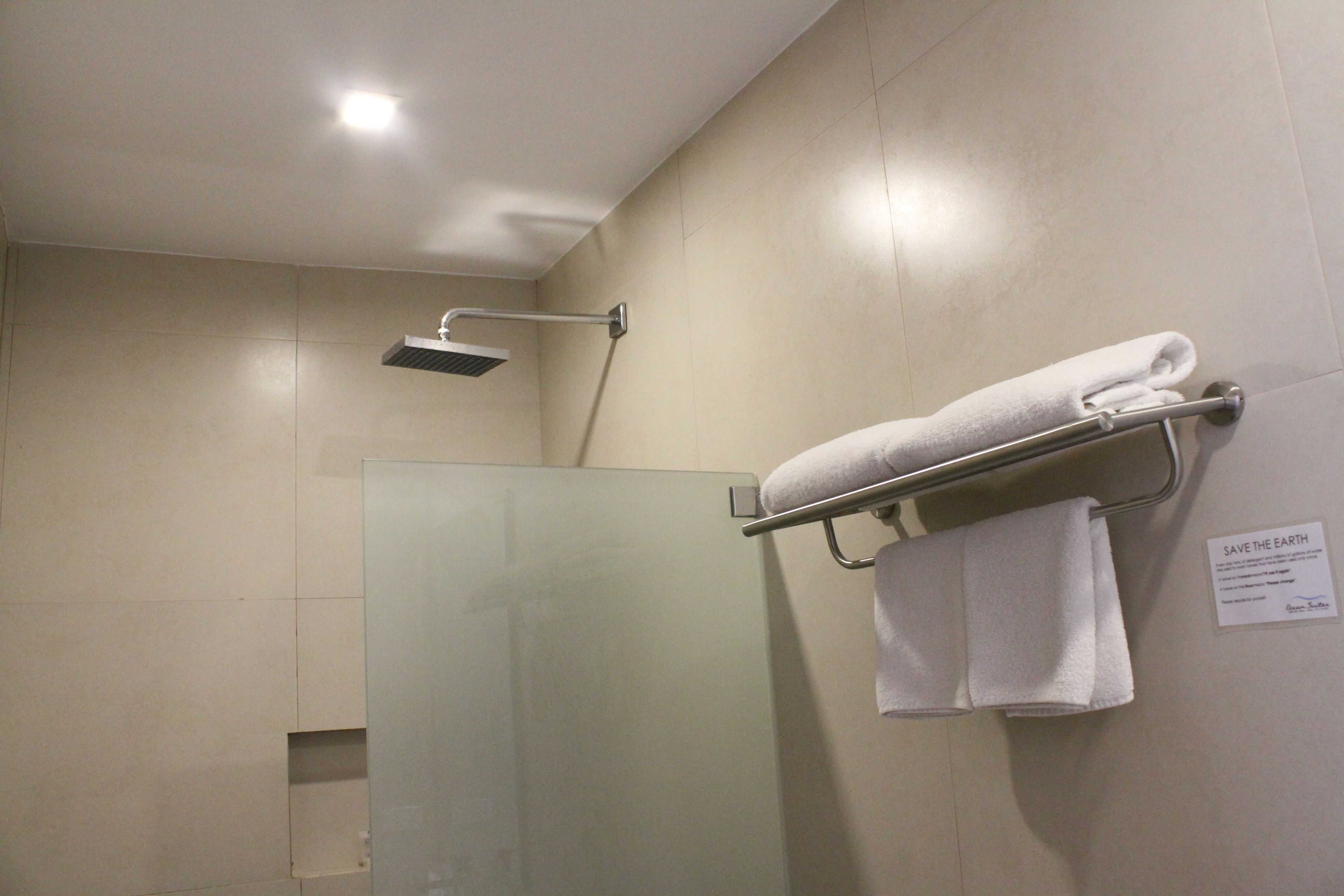 Un baño moderno con cabina de ducha de vidrio, un perchero con una toalla doblada y un cartel que dice 'SAVE THE EARTH' en la pared.