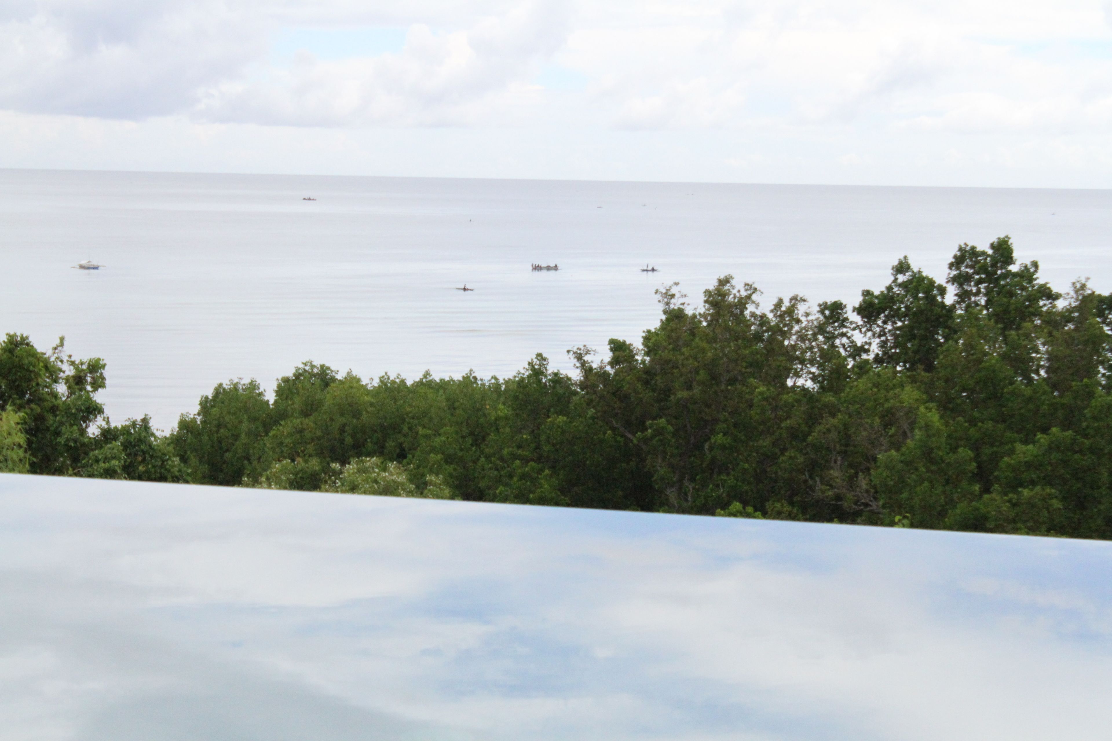 Vista costera con mar tranquilo, varias embarcaciones y vegetación verde exuberante al frente.