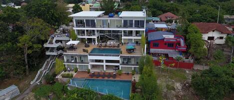 Un edificio de varios pisos con piscina en la azotea, zona de estar al aire libre y una escalera que sube a los niveles superiores.