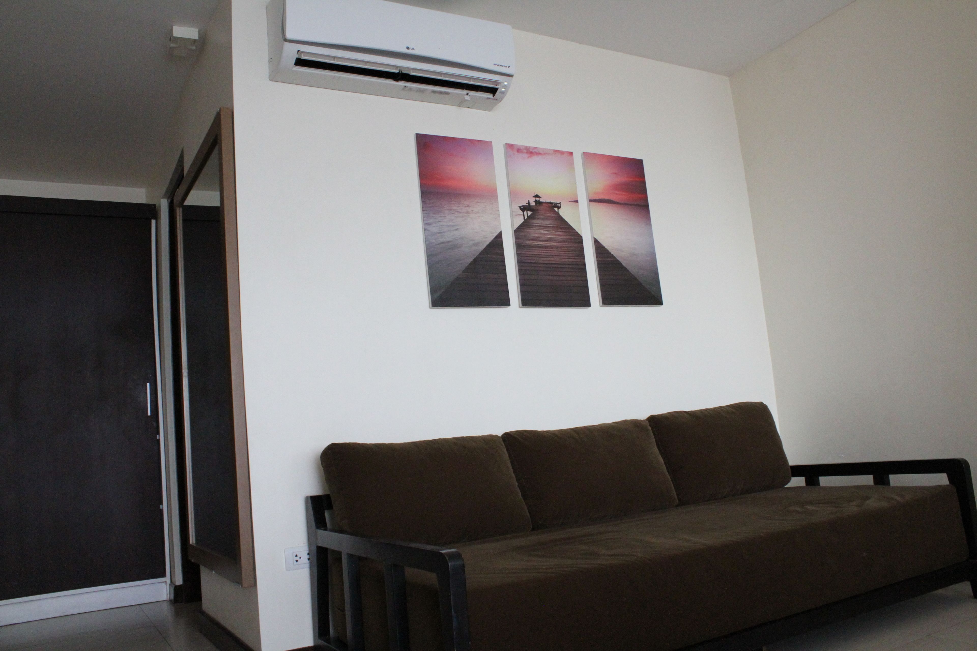 A room with a brown sofa, a wall-mounted air conditioner, and three sunset pictures on the wall.
