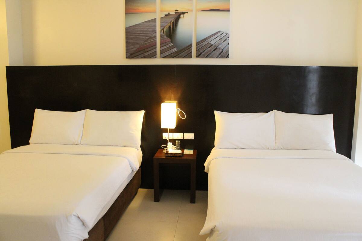 Ein Hotelzimmer mit zwei Betten, einem Nachttisch mit Lampe und einem Wandbild von einem Steg.