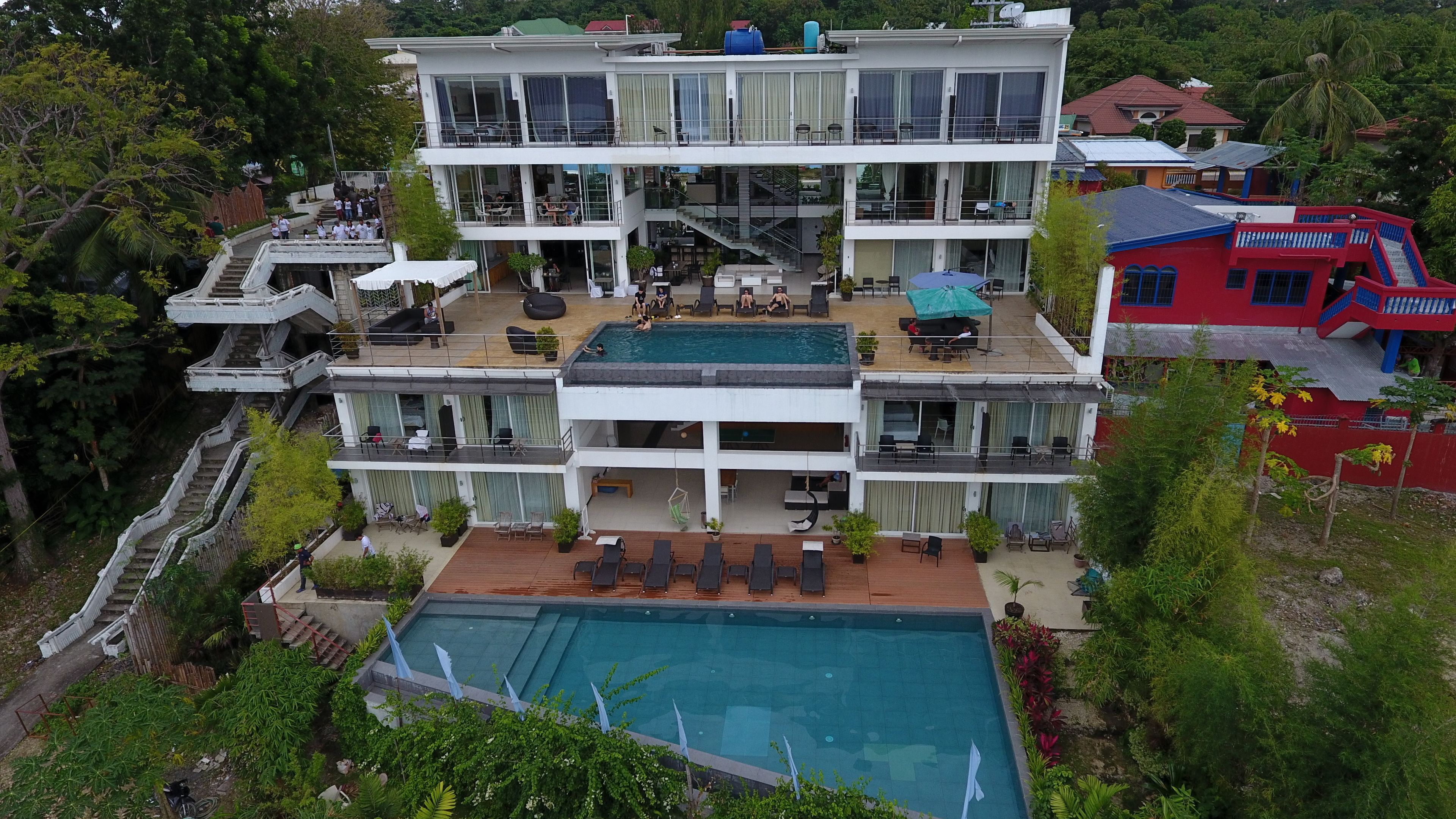 A multi-story hotel with a swimming pool, outdoor seating, and a staircase leading to the upper floors.
