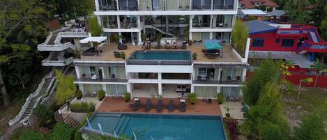 A multi-story hotel with a swimming pool, outdoor seating, and a staircase leading to the upper floors.