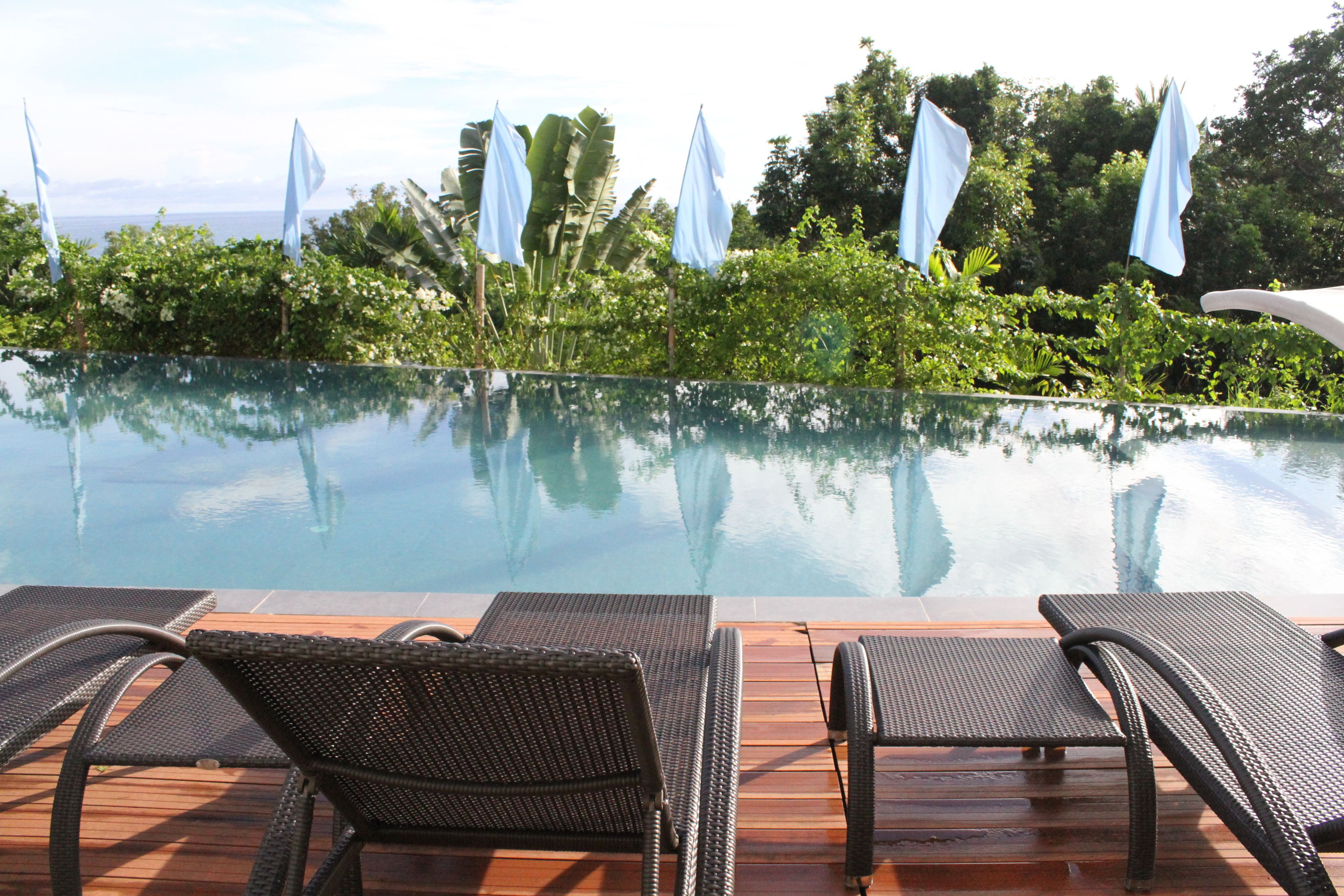 Una piscina infinita con agua cristalina, rodeada de exuberante vegetación y banderas blancas.