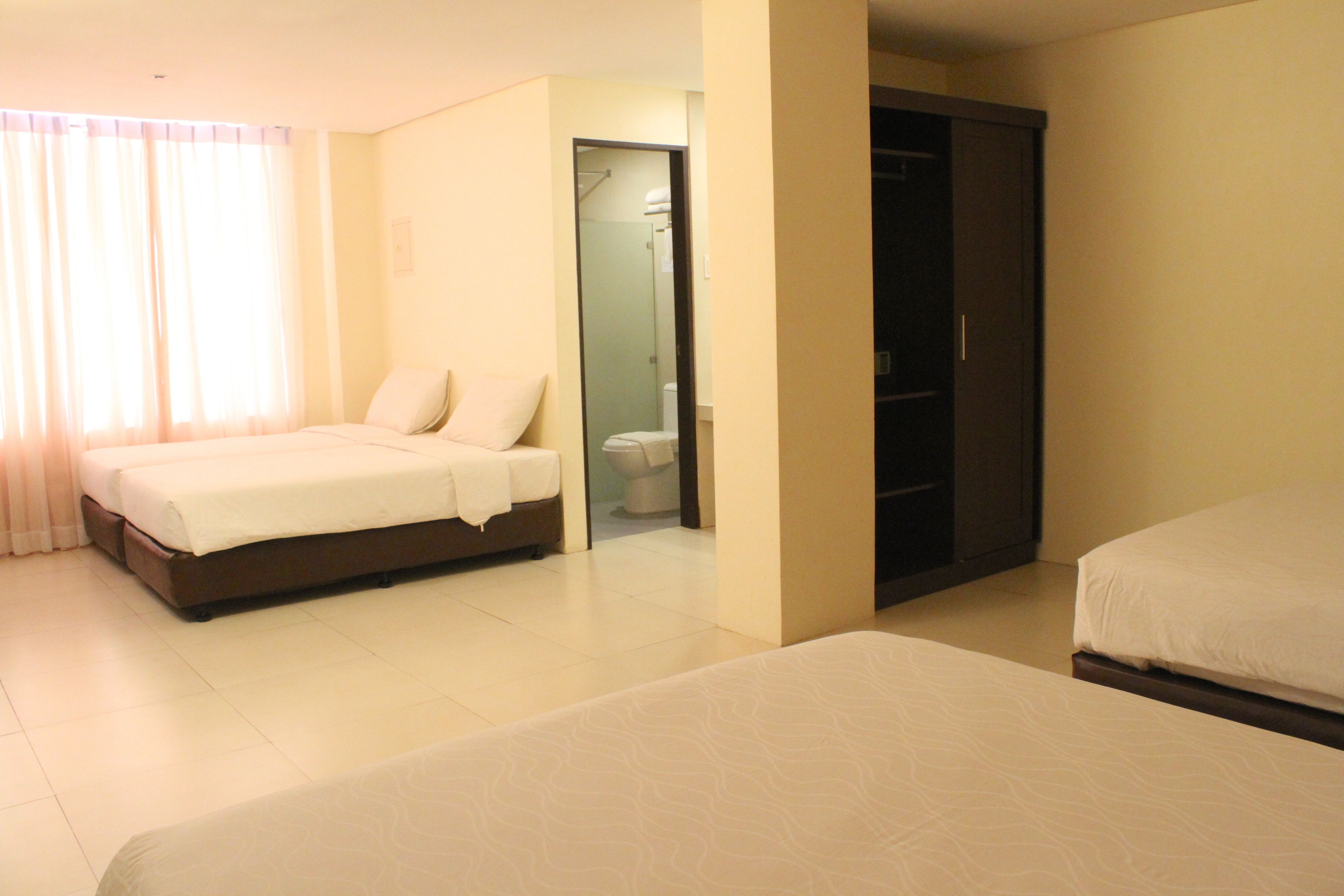 A hotel room with two beds, a bathroom with a toilet and shower, and a wardrobe.