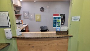 Un mostrador de recepción con un reloj, un cartel que indica los horarios de entrada y salida, y un anuncio para servicios de lavandería.