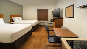 Habitación de hotel con dos camas, un escritorio, una silla, un televisor y un tablón de corcho en la pared.