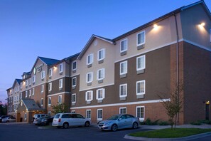A multi-story hotel with a brick facade, multiple windows, and a parking lot with several cars. - WoodSpring Suites Louisville Jeffersontown (Louisville)