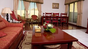 A living room with a sofa, a wooden coffee table with a vase of flowers, a dining table with chairs, and a large window with curtains. - Green Mubazzarah Chalets (Al Ain)