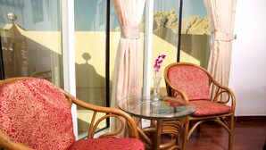 A room with two wicker chairs with red patterned upholstery, a glass table, and a vase with a purple orchid. - Green Mubazzarah Chalets (Al Ain)