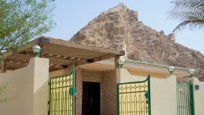 A building with a stone facade, green metal gates, and a wooden pergola. - Green Mubazzarah Chalets (Al Ain)