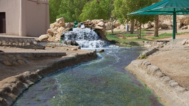 A water feature with a small waterfall, surrounded by rocks and greenery. - Green Mubazzarah Chalets (Al Ain)