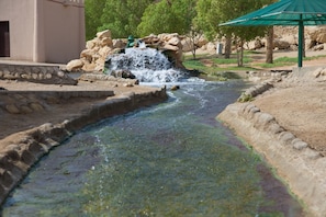 A water feature with a small waterfall, surrounded by rocks and greenery. - Green Mubazzarah Chalets (Al Ain)