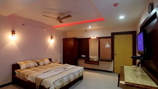 A bedroom with a bed, wardrobe, mirror, television, and ceiling fan. - Grand Elite hotel (Hyderabad)