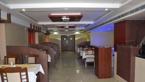 A restaurant with booths and tables, a central walkway, and a modern ceiling design. - Grand Elite hotel (Hyderabad)