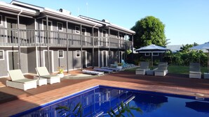 A modern building with a pool area, including lounge chairs and umbrellas. - Travellers Point Hotel (Apia)