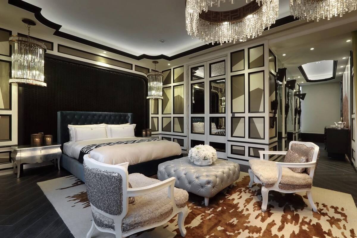 Un dormitorio moderno con una cama grande, un cabecero capitonado, una araña y una alfombra de piel de vaca.
