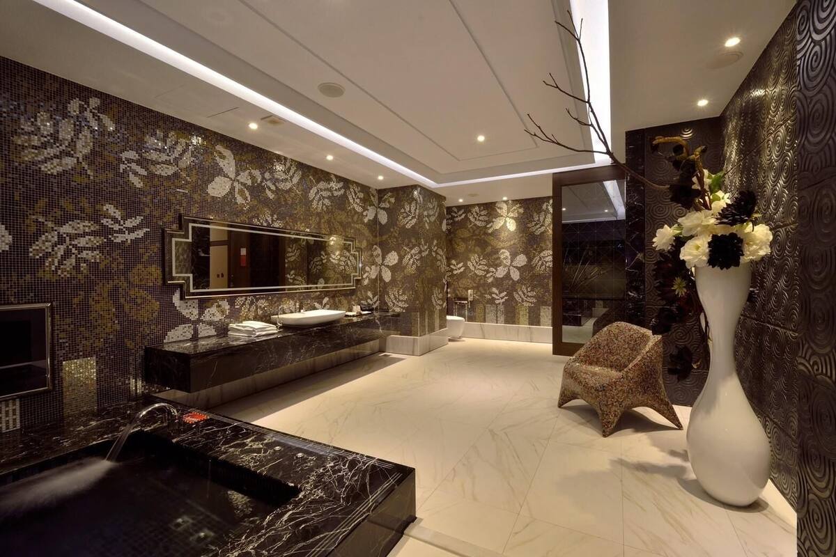 Un baño moderno con un espejo grande, un lavabo de mármol negro y una pared con mosaicos florales.