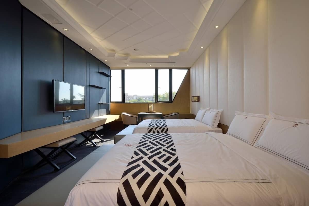 Una habitación de hotel moderna con dos camas, un escritorio, un televisor y un amplio ventanal con vistas a la ciudad.