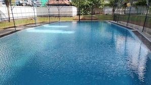 A rectangular swimming pool with a tiled edge, surrounded by a fence and a grassy area with trees. - H&A Guest House (Malacca City)