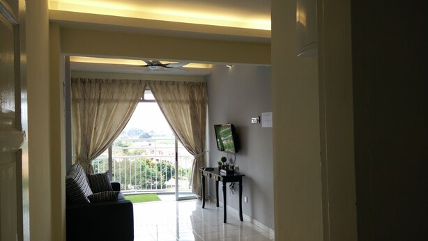 A living room with a sofa, a TV on a stand, and a view of greenery outside. - H&A Guest House (Malacca City)
