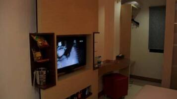 A modern hotel room with a flat-screen TV mounted on the wall, a small red ottoman, and a minimalist design.