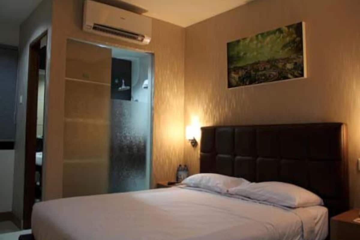 A hotel room with a bed, a nightstand, a wall-mounted air conditioner, and a painting.