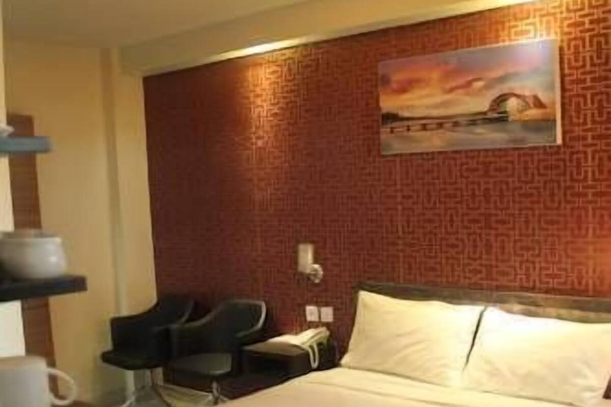 A hotel room with a large bed, a desk with a chair, a painting on the wall, and a patterned wall design.