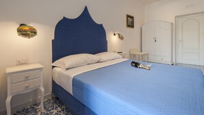 A bedroom with a bed, a nightstand, a dresser, and a wall-mounted light fixture. - Surriento Suites (Sorrento)
