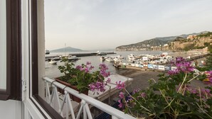 A coastal view from a balcony with potted plants, a marina with boats, and a distant mountain. - Surriento Suites (Sorrento)
