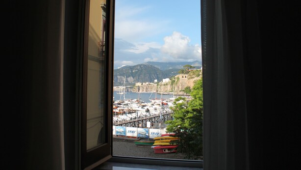 A view from a window overlooking a marina with boats and a mountainous backdrop. - Surriento Suites (Sorrento)