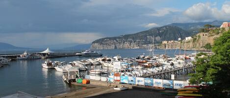 A marina with boats docked, a pier extending into the water, and a mountainous backdrop.