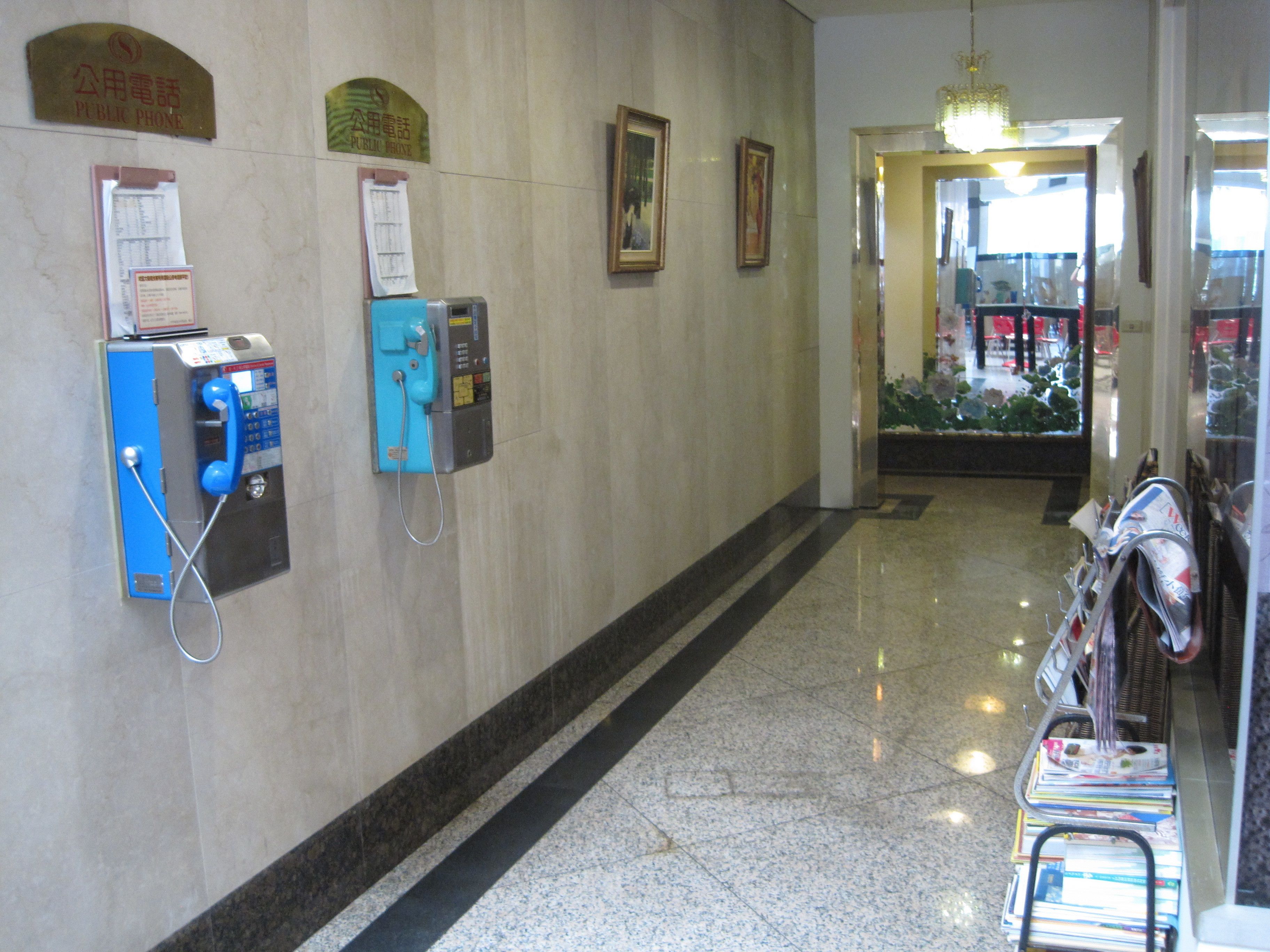 A hallway with public phones, a bulletin board, and a magazine rack.