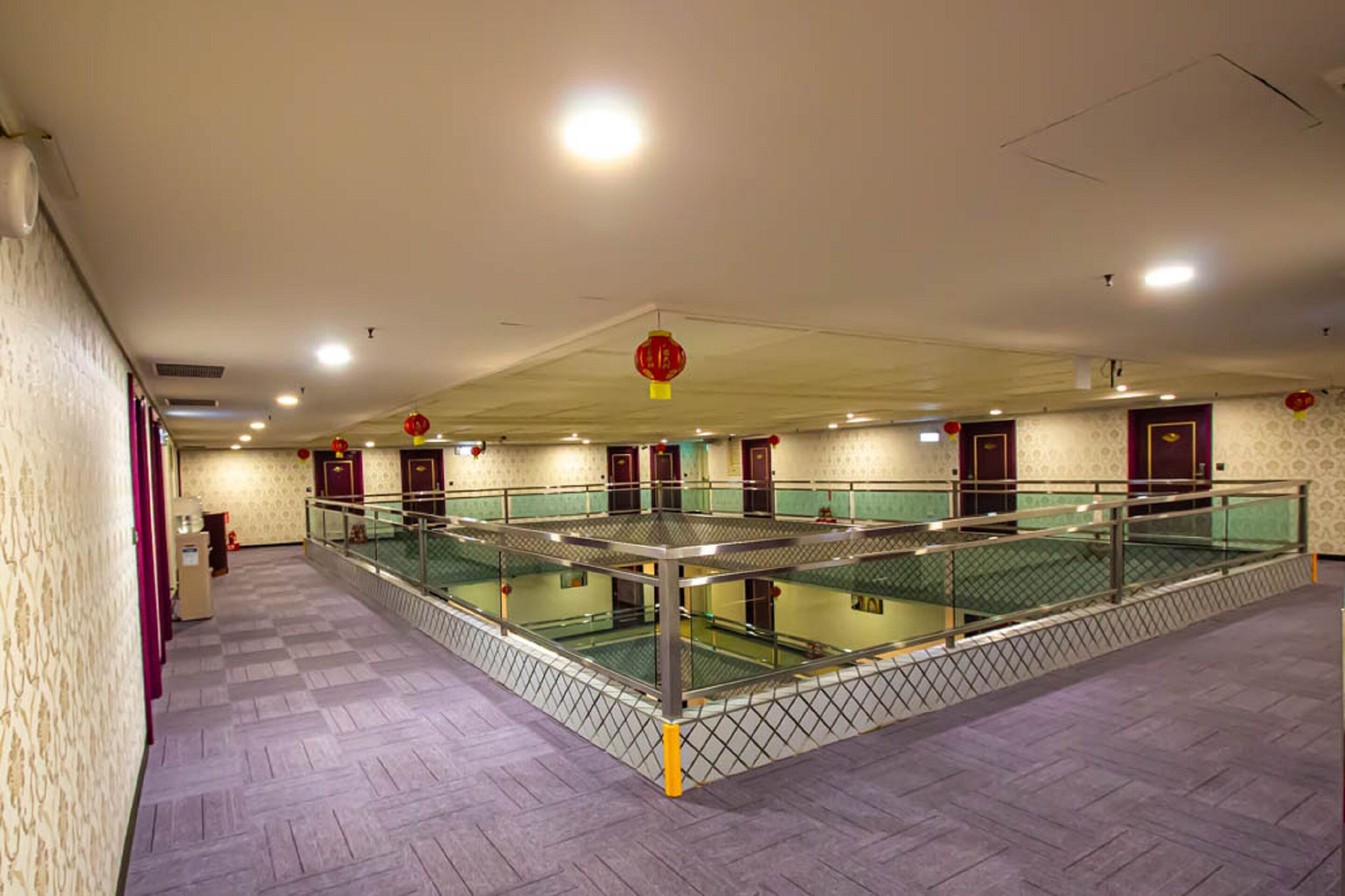 A spacious indoor area with a central glass railing, multiple doors, and red lanterns.