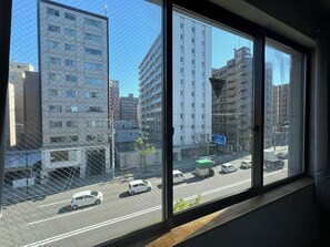 A view through a window with a metal grid, overlooking a street with cars and buildings.