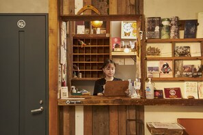 A person at a wooden counter with a laptop, surrounded by books and various items.