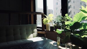 A cozy seating area with a cushioned bench and a small table, near a window with a view of buildings. - Untapped Hostel (Sapporo)