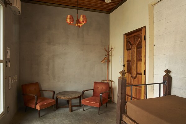 A room with a wooden door, a round table, two armchairs, and a ceiling light fixture.