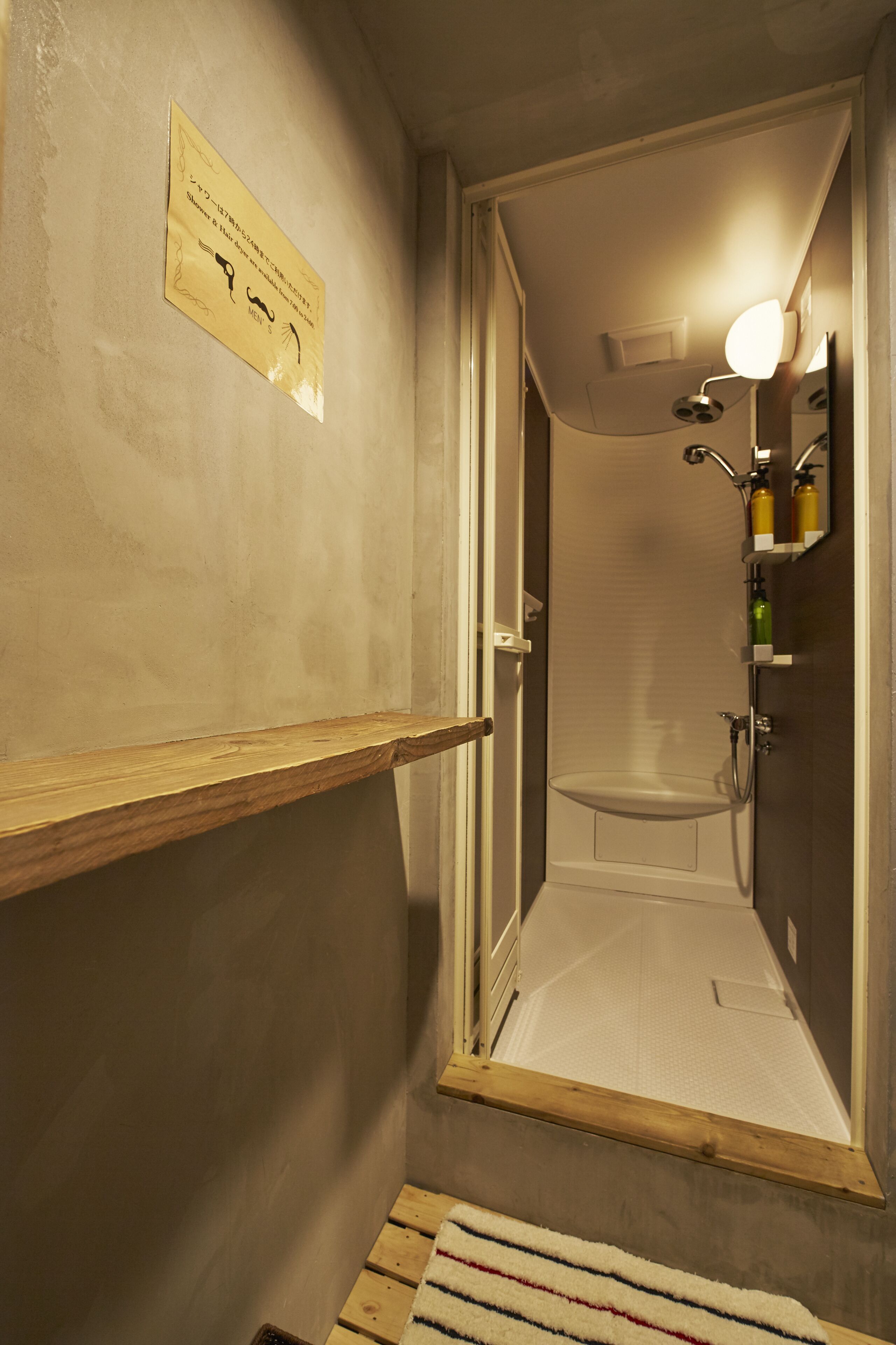 A narrow hallway leading to a bathroom with a shower, a wooden shelf, and a sign on the wall.