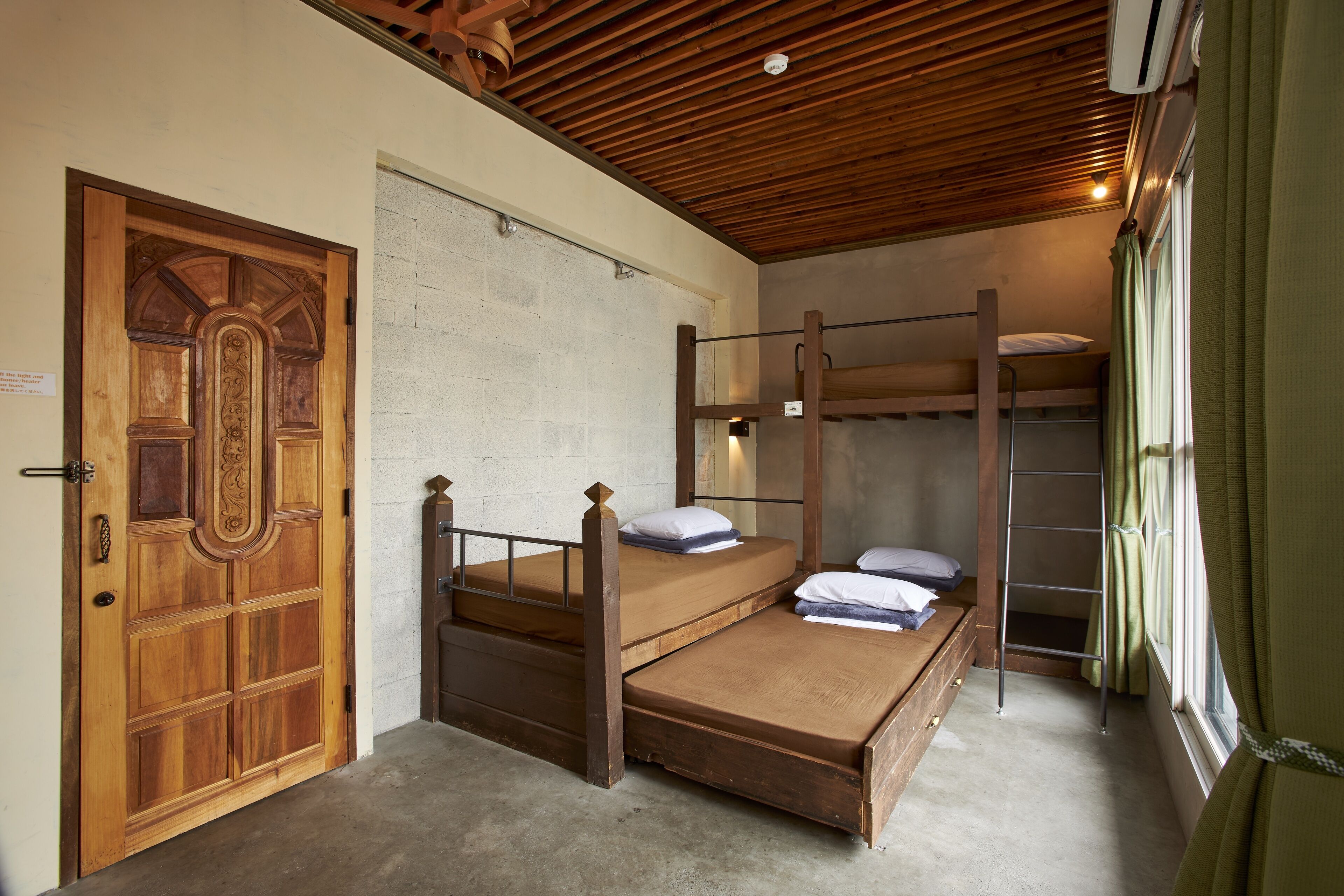 A room with a wooden door, bunk beds, a ladder, and a window with curtains.