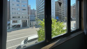 A view through a window with a metal grid, overlooking a street with buildings and a white van. - Untapped Hostel (Sapporo)