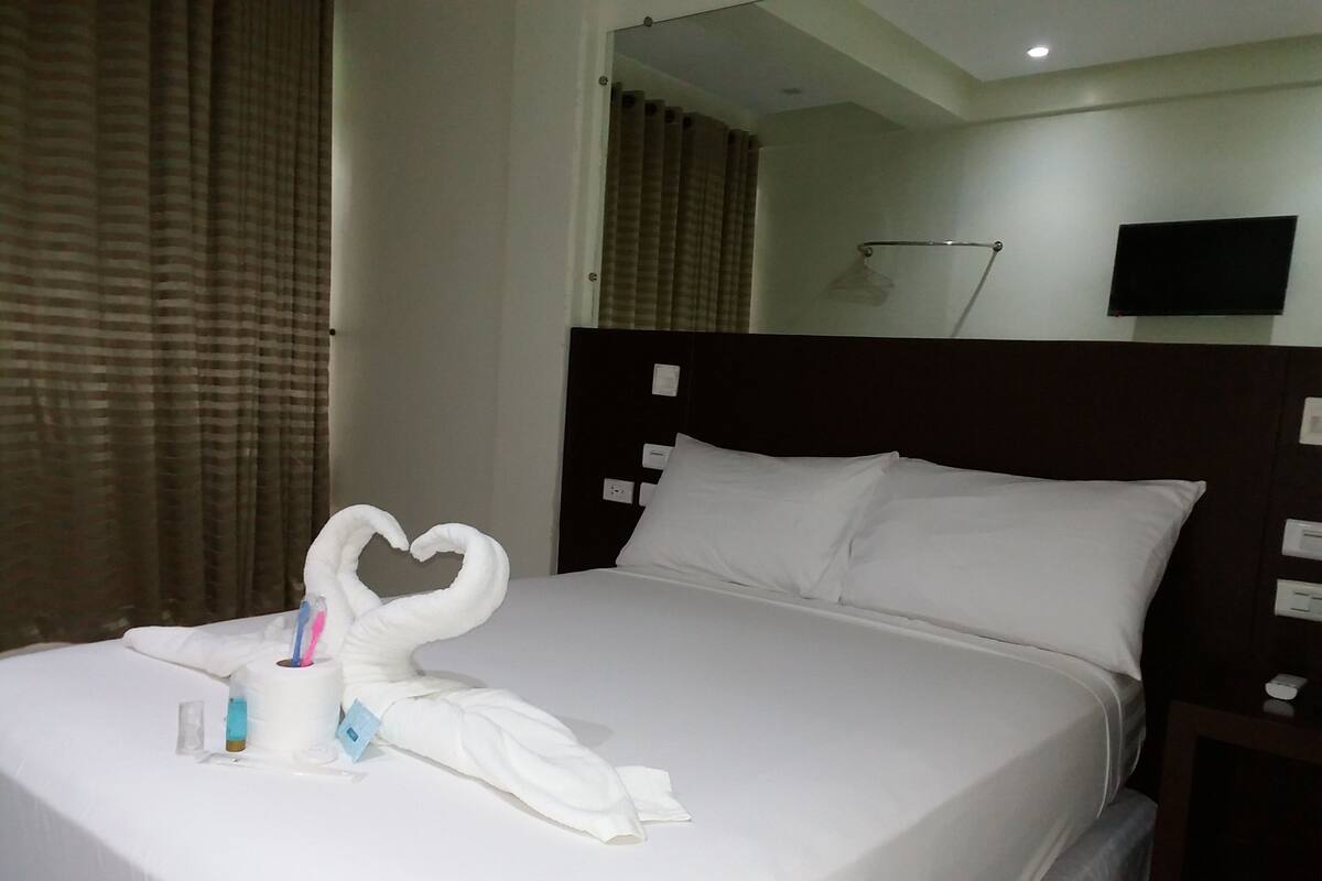 A neatly made bed with white linens and a heart-shaped towel arrangement.