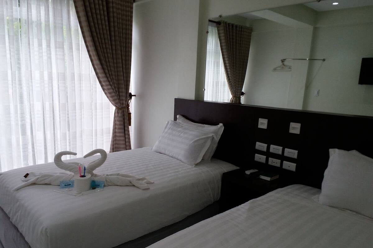 A hotel room with two beds, a large mirror, and a nightstand with a phone and a book.