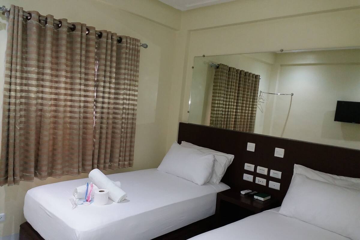 A hotel room with a single bed, a bedside table with a remote control, and a mirror on the wall.