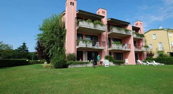 A multi-story building with balconies, a well-maintained lawn, and a clear sky.