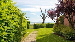 A pathway leading to a body of water, surrounded by lush greenery and a large tree. - Virgilio Residence (Sirmione)
