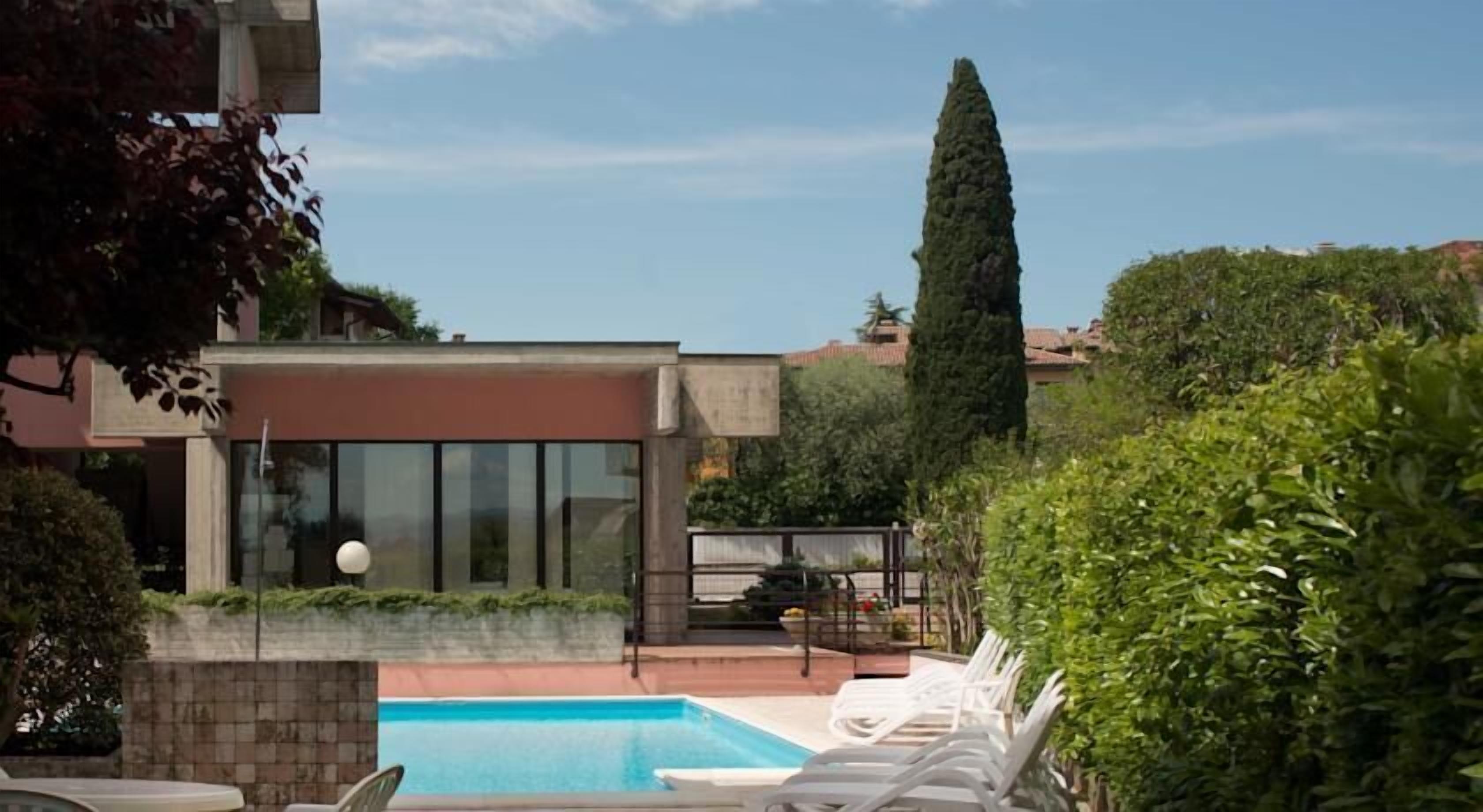Un edificio moderno con una piscina, sdraio e un alto albero.