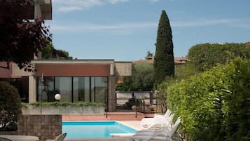 Un edificio moderno con una piscina, sdraio e un alto albero.