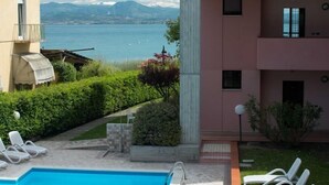A pool area with lounge chairs, a view of a lake, and a building with a balcony. - Virgilio Residence (Sirmione)
