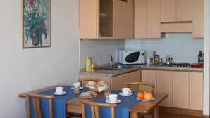 A small kitchen with a microwave, sink, and stove. There is a dining table with chairs and a blue tablecloth. - Virgilio Residence (Sirmione)